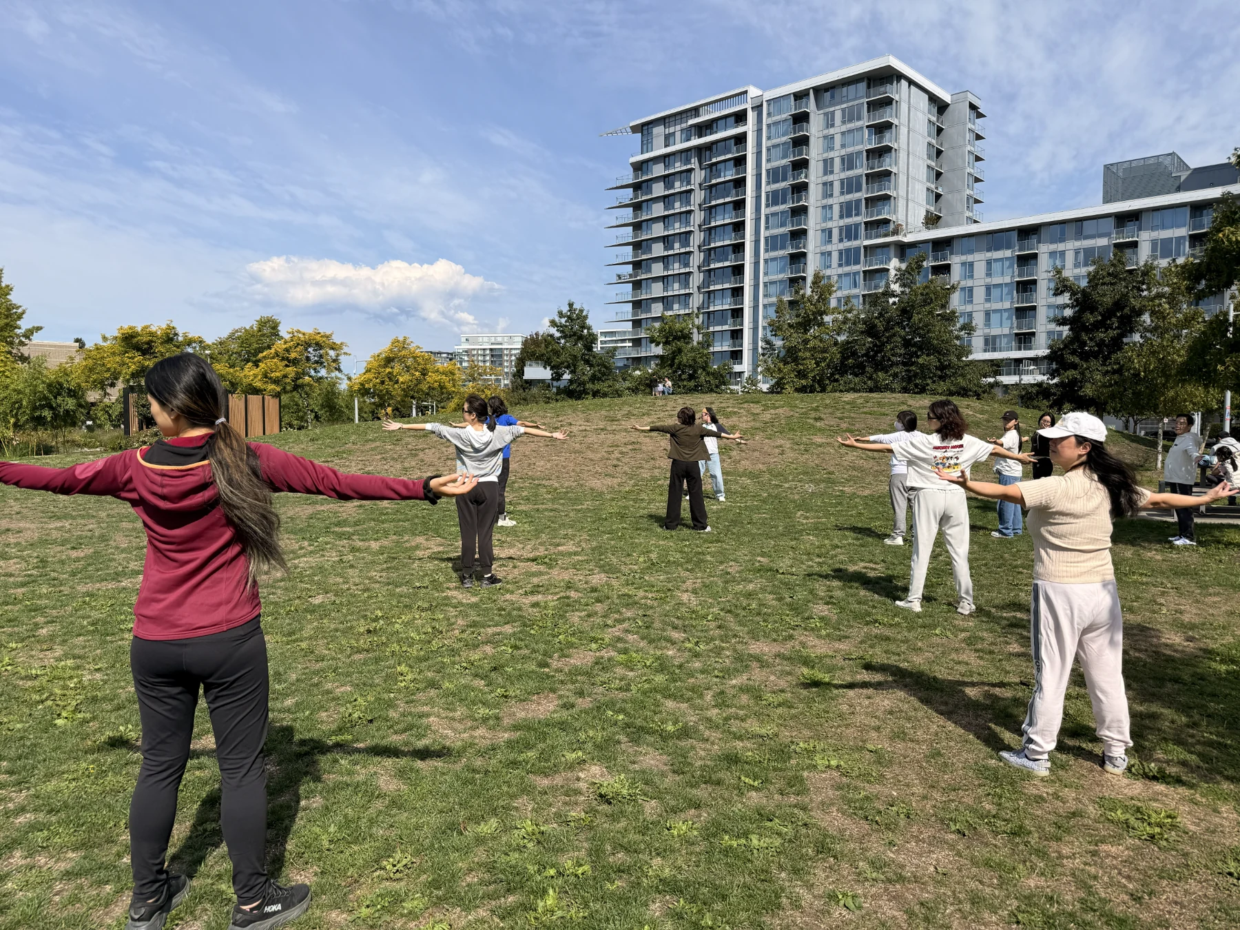 Participants extending their arms during a Baduanjin exercise on the park lawn.