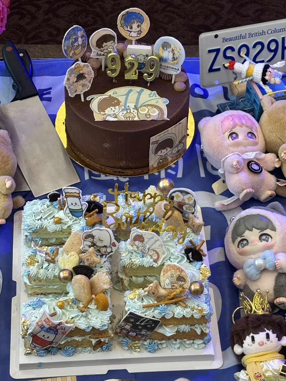 Birthday cakes and plush toys arranged on a blue cloth.