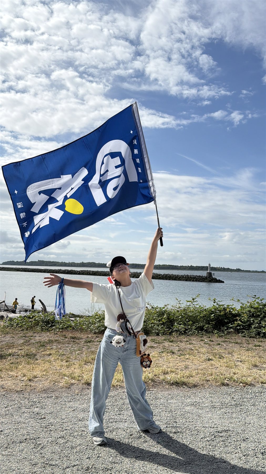 A Vancouver Shengmi member joyfully waving a Zhou Shen fan flag by the water.